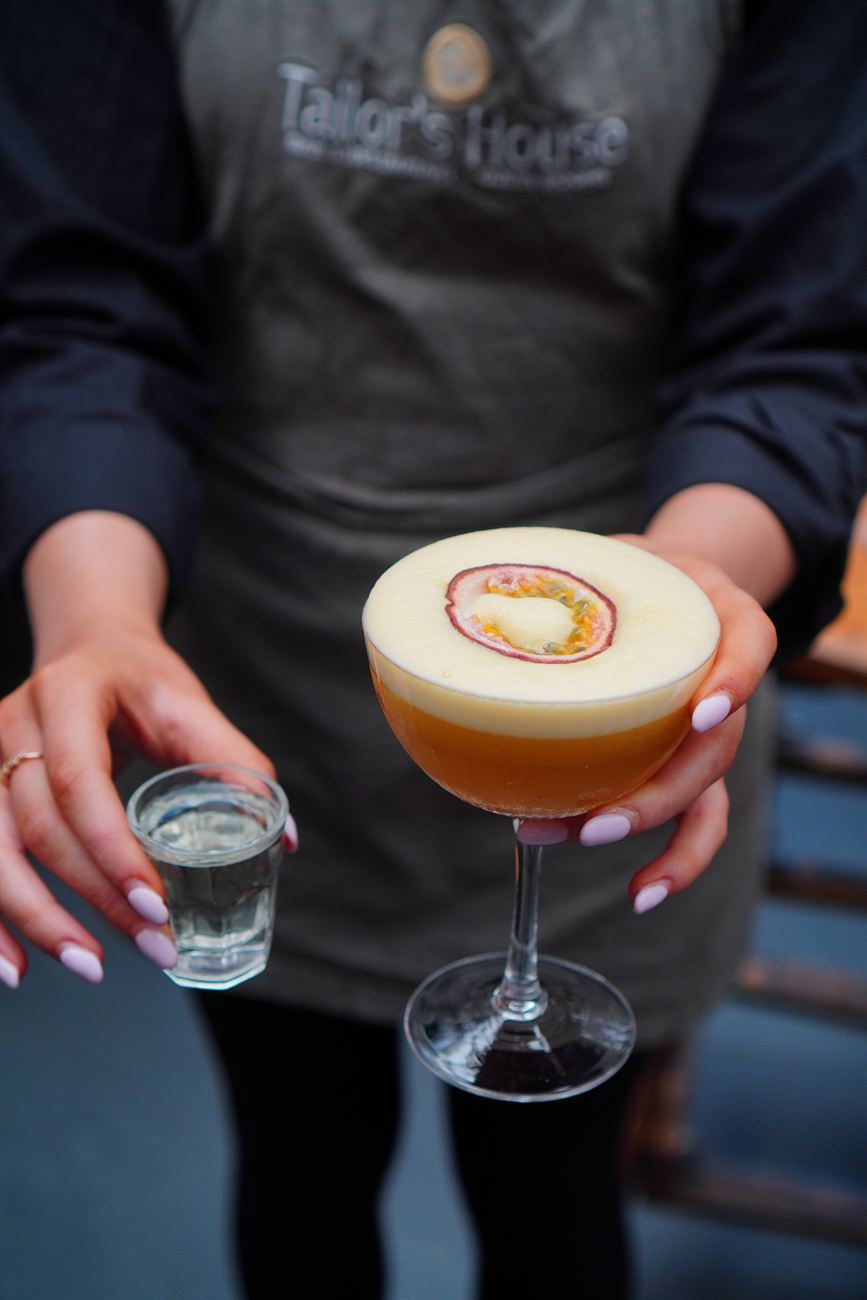 A passionfruit martini served with a shot, in a branded Tailor's House apron