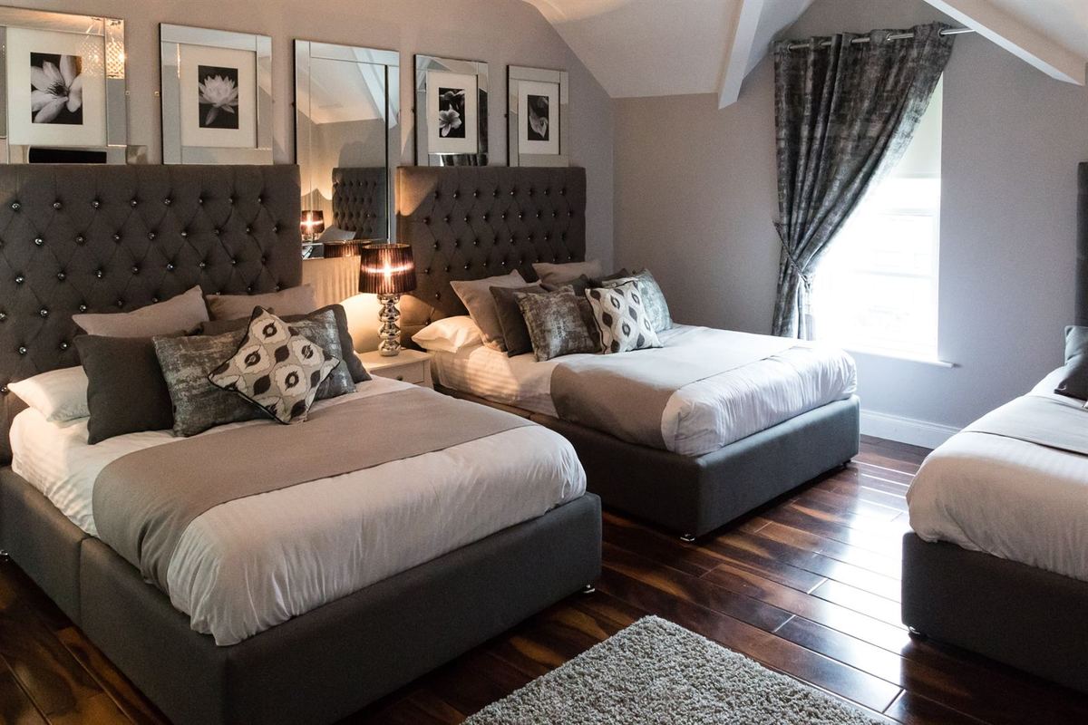 Spacious family guest room with two double beds and a single, grey velvet tufted headboards and dark wood floor